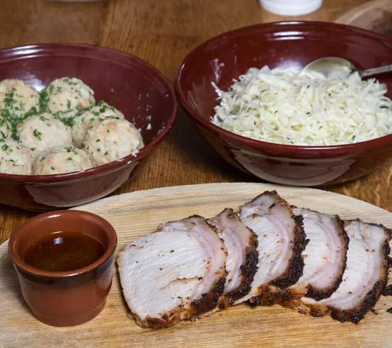 Scheiben Schweinebraten mit Soße, Knödel und Sauerkraut in Schalen
